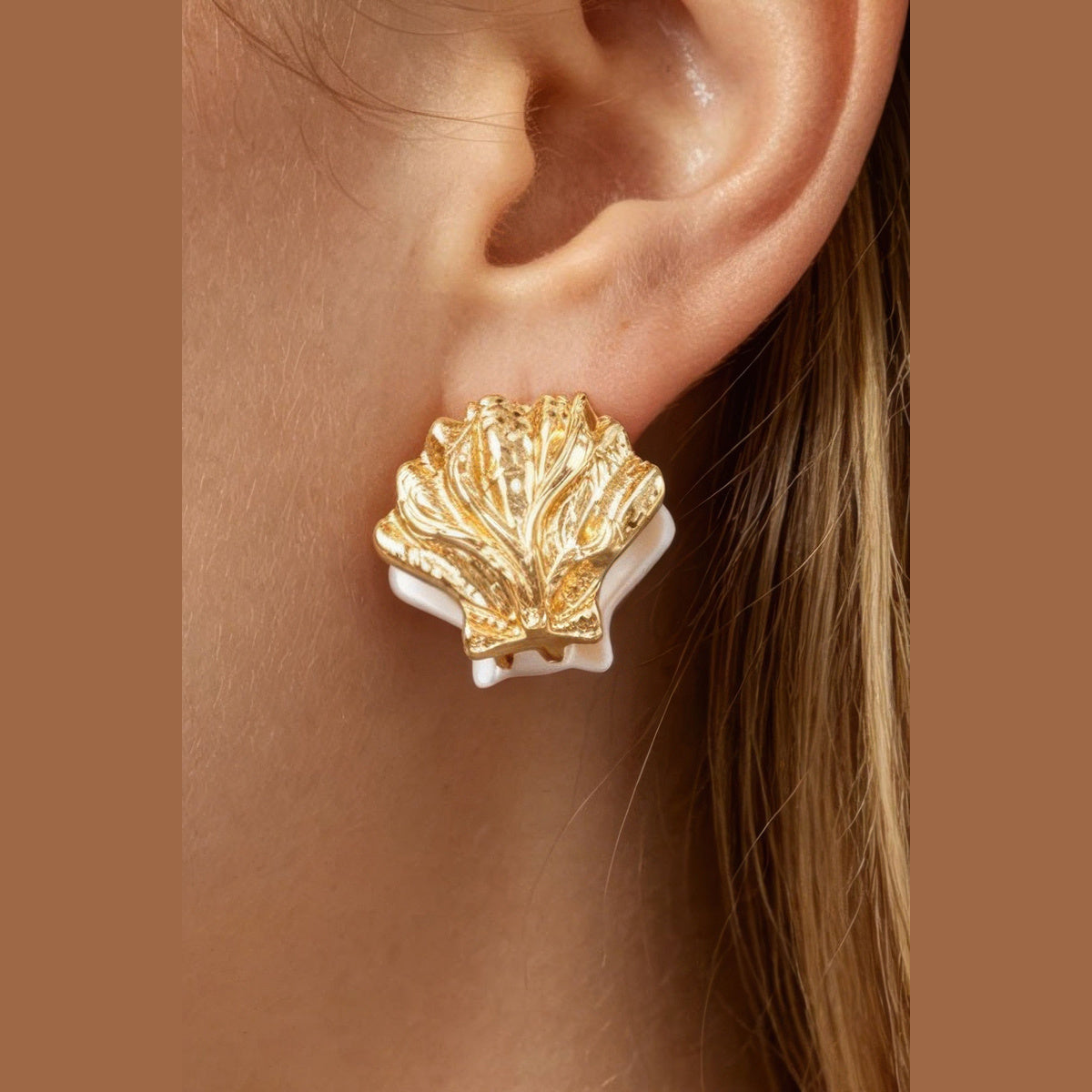 Two-Tone Clamshell Earrings in gold and pearl white, close-up worn on the ear