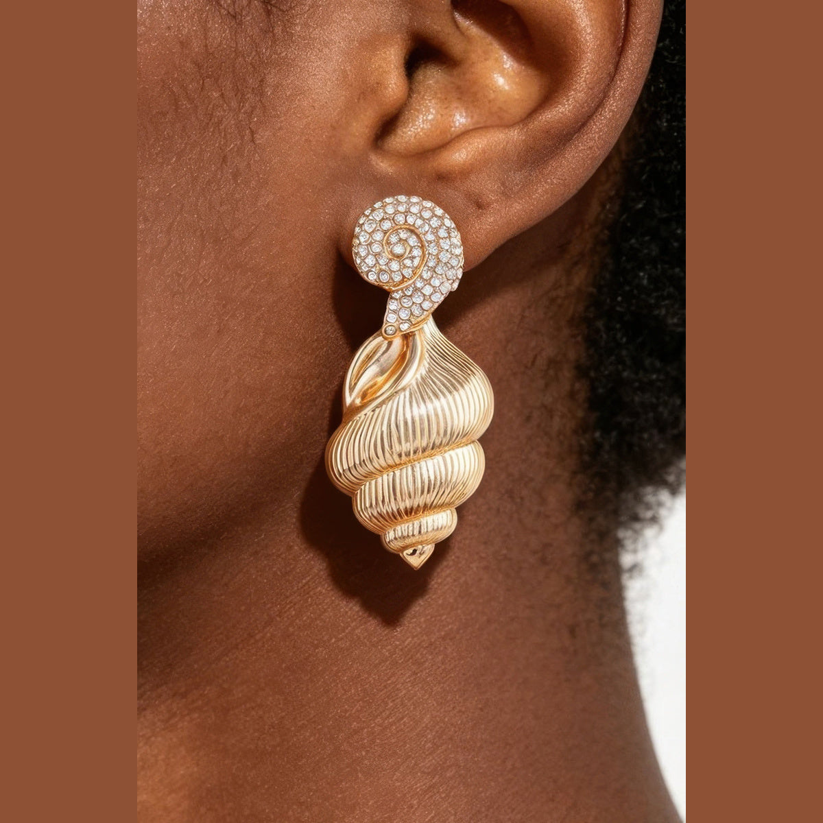 Jeweled Conch Shell Drop Earrings in gold with clear stones, close-up worn on the ear