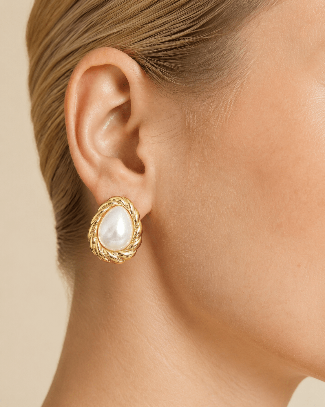 Close-up of a model wearing teardrop pearl-effect stud earrings with a twisted gold-tone frame