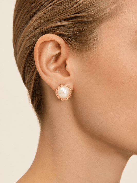 Close-up of a model wearing round pearl-effect stud earrings with a braided gold-tone frame