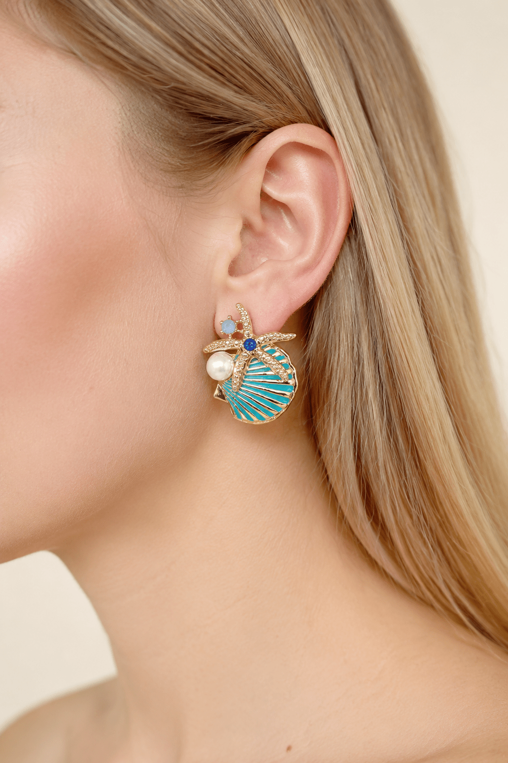 Close-up of a model wearing aqua starfish and shell statement earrings with pearl-effect accents