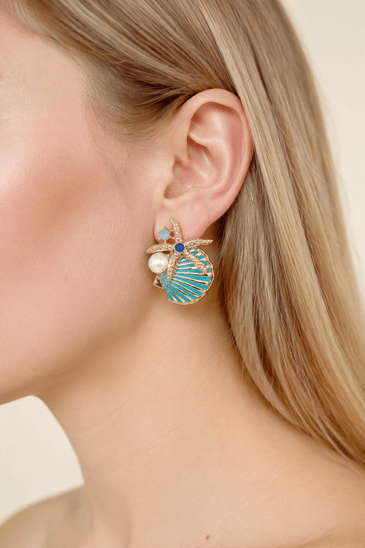 Close-up of a model wearing aqua starfish and shell statement earrings with pearl-effect accents