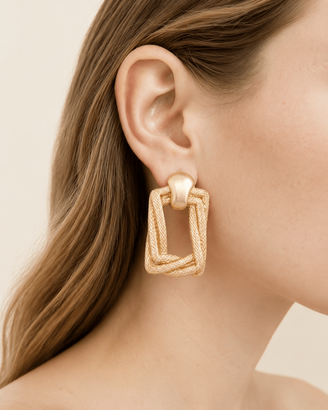 Close-up of a model wearing gold-tone braided door-knocker earrings