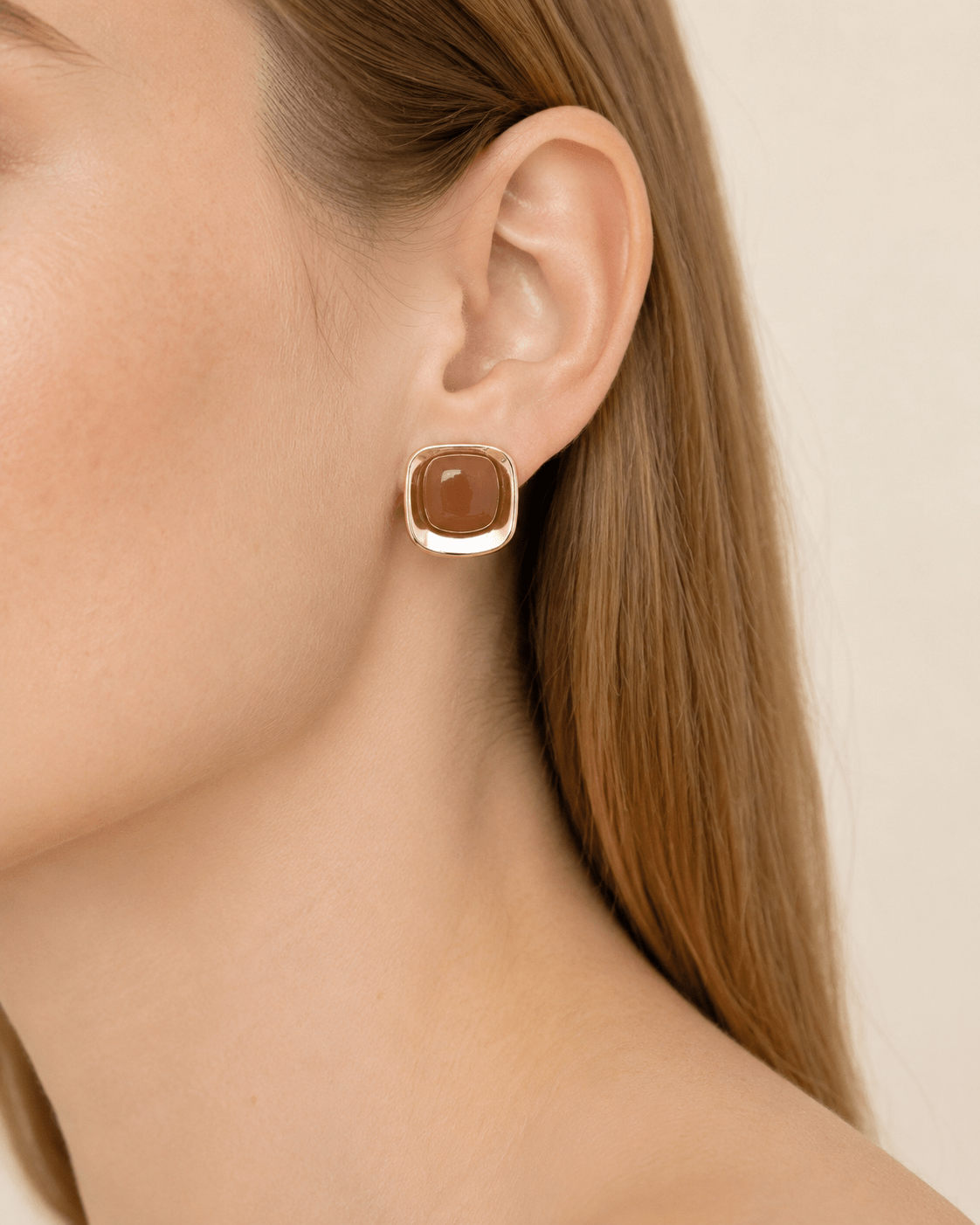 Close-up of a model wearing polished gold-tone square stud earrings with a marbled center