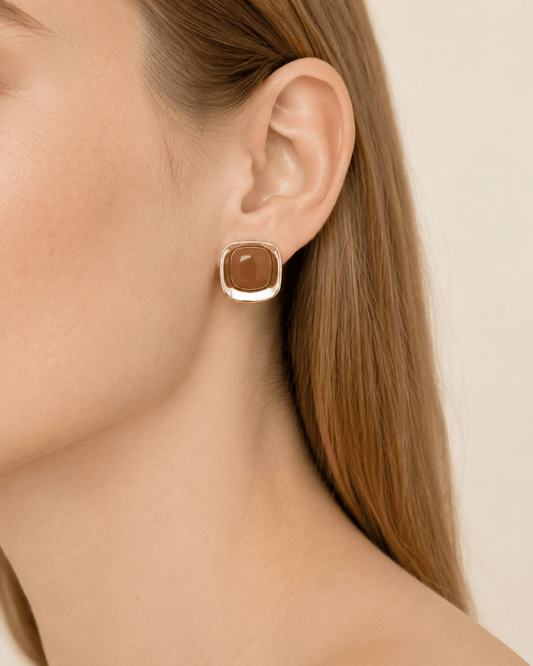 Close-up of a model wearing polished gold-tone square stud earrings with a marbled center