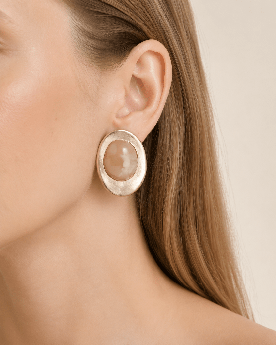 Close-up of a model wearing matte gold-tone oval earrings with a marbled stone-effect center