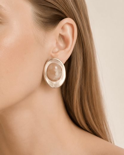 Close-up of a model wearing matte gold-tone oval earrings with a marbled stone-effect center