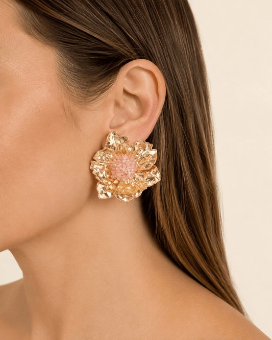 Close-up of a model wearing oversized gold-tone flower earrings with pink beaded centers
